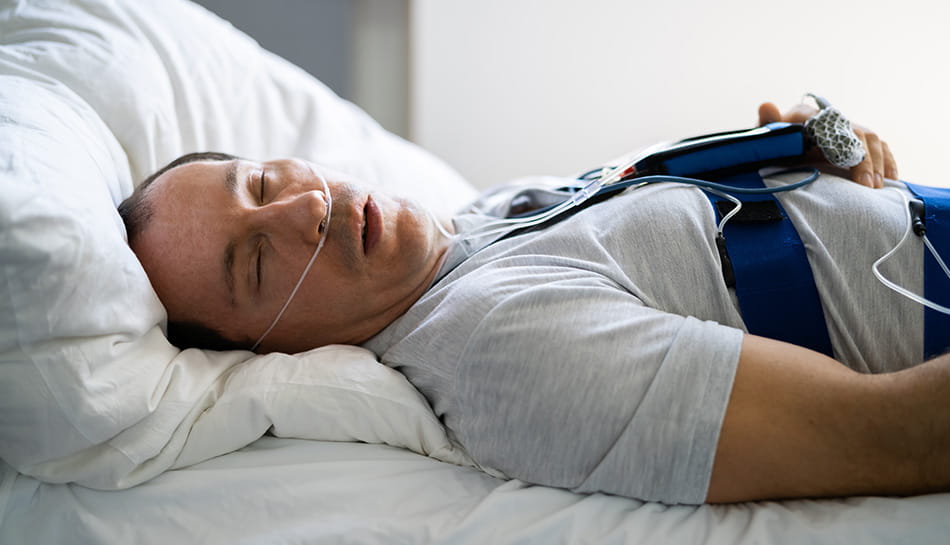 Man undergoing a sleep study with monitoring equipment while sleeping in a medical setting.
